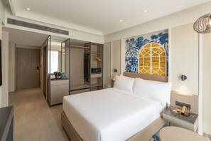 Una habitación de hotel con una cama grande, un vestidor, una kitchenette pequeña y un mural decorativo en la pared.