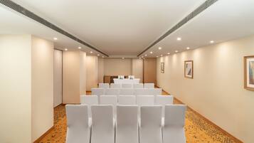 A conference room with rows of white chairs, a table with a white tablecloth, and framed pictures on the walls.