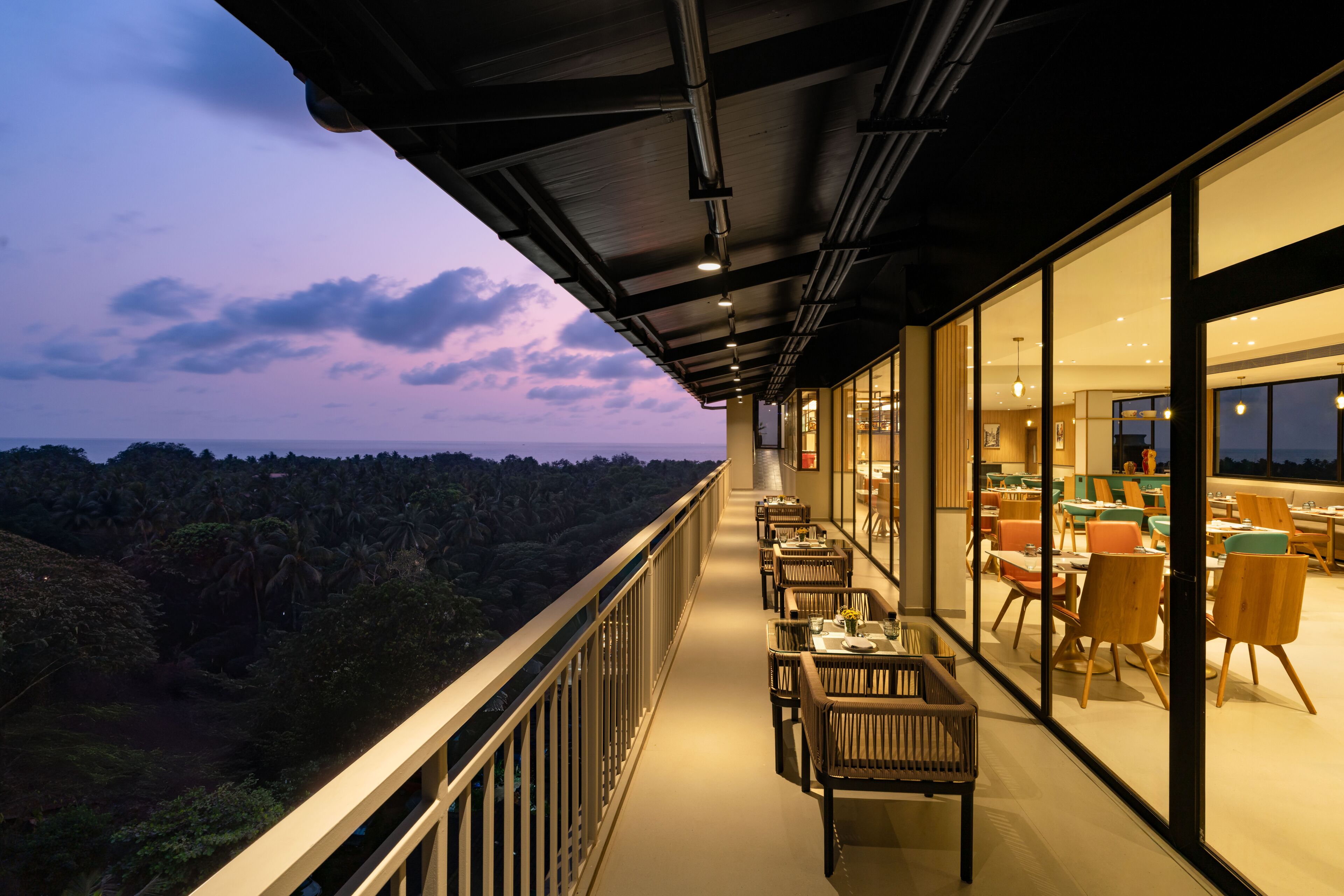A balcony with tables and chairs, overlooking a forested landscape.