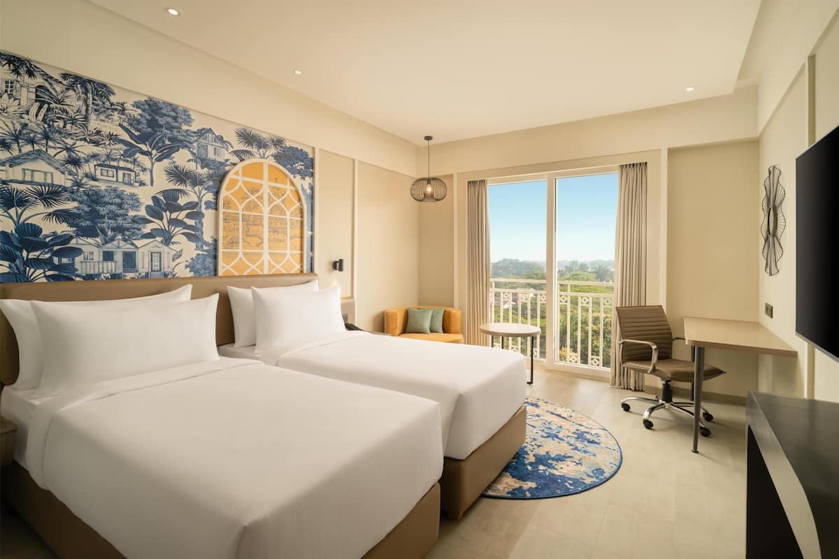 A hotel room with two beds, a balcony with a view, a desk, and a TV.