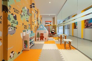 Un'area giochi per bambini con decorazioni murali didattiche, una casetta e un angolo relax con tavoli e sedie.