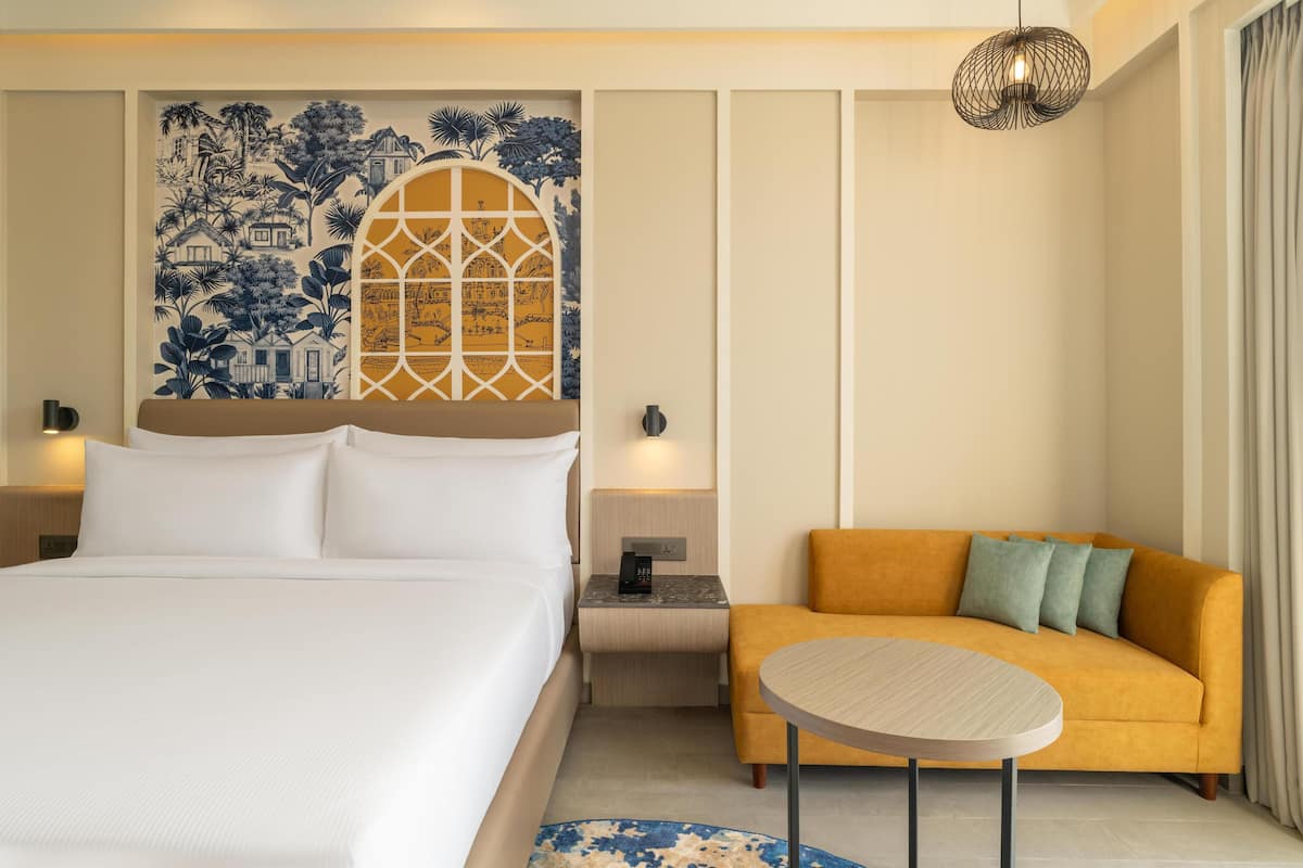 A hotel room with a bed, a sofa, a round table, and a decorative wall with a window.