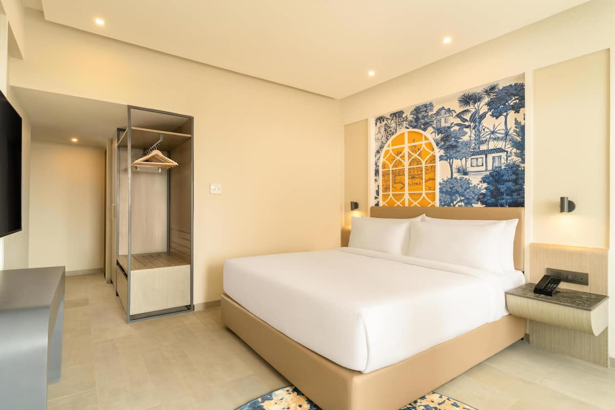 A hotel room with a bed, a wardrobe, a desk, and a wall with a blue and yellow mural.