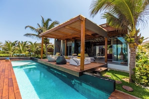 Un espace moderne aménagé au bord de la piscine, avec une terrasse en bois, des sièges et un patio couvert.