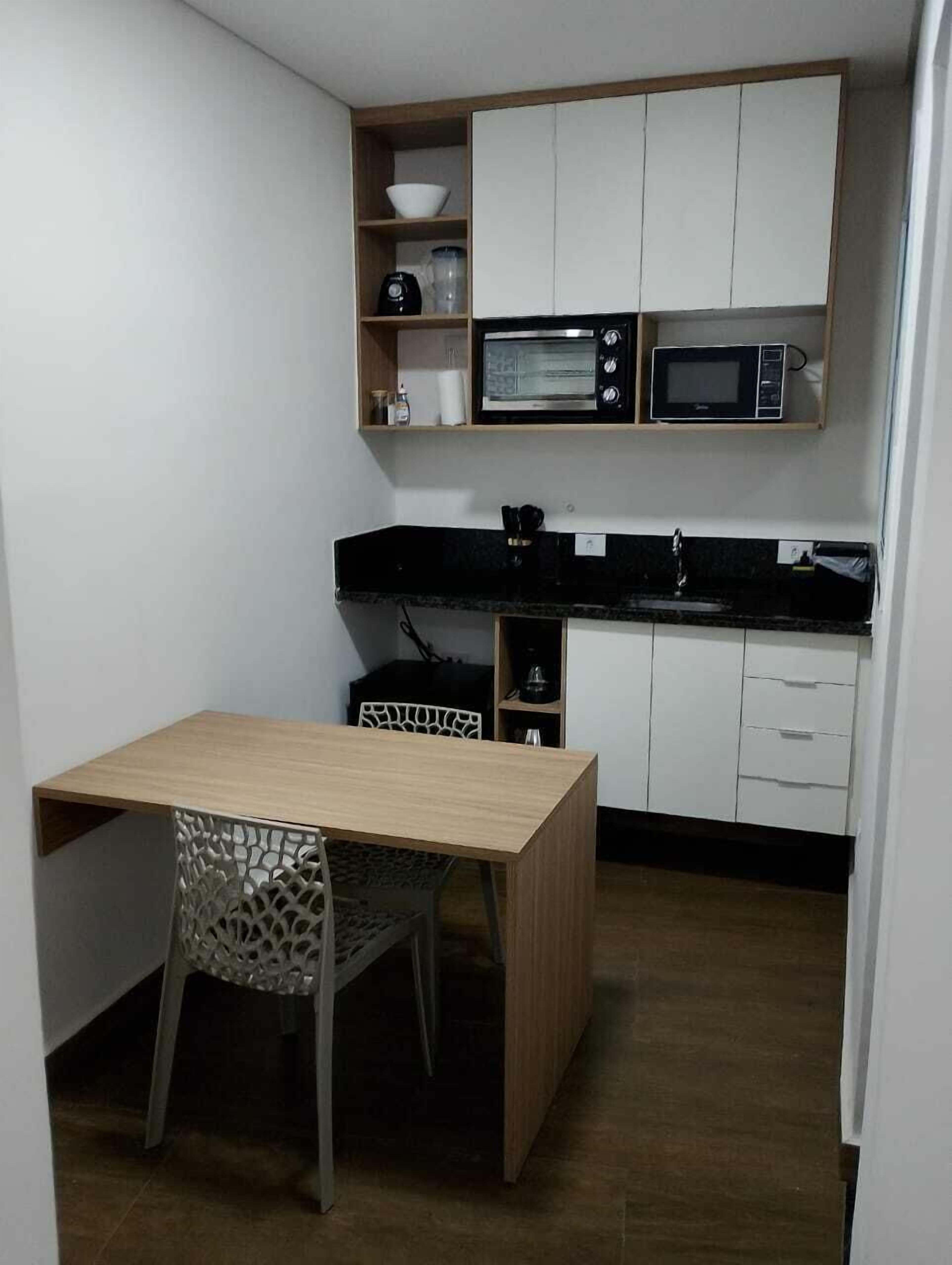 A compact kitchen with a wooden table and a chair, white cabinets, and two microwaves.