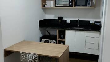 A compact kitchen with a wooden table and a chair, white cabinets, and two microwaves.