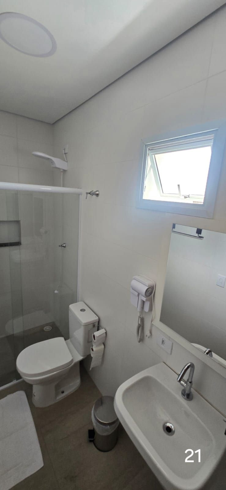 A bathroom with a toilet, shower, sink, and a small window.