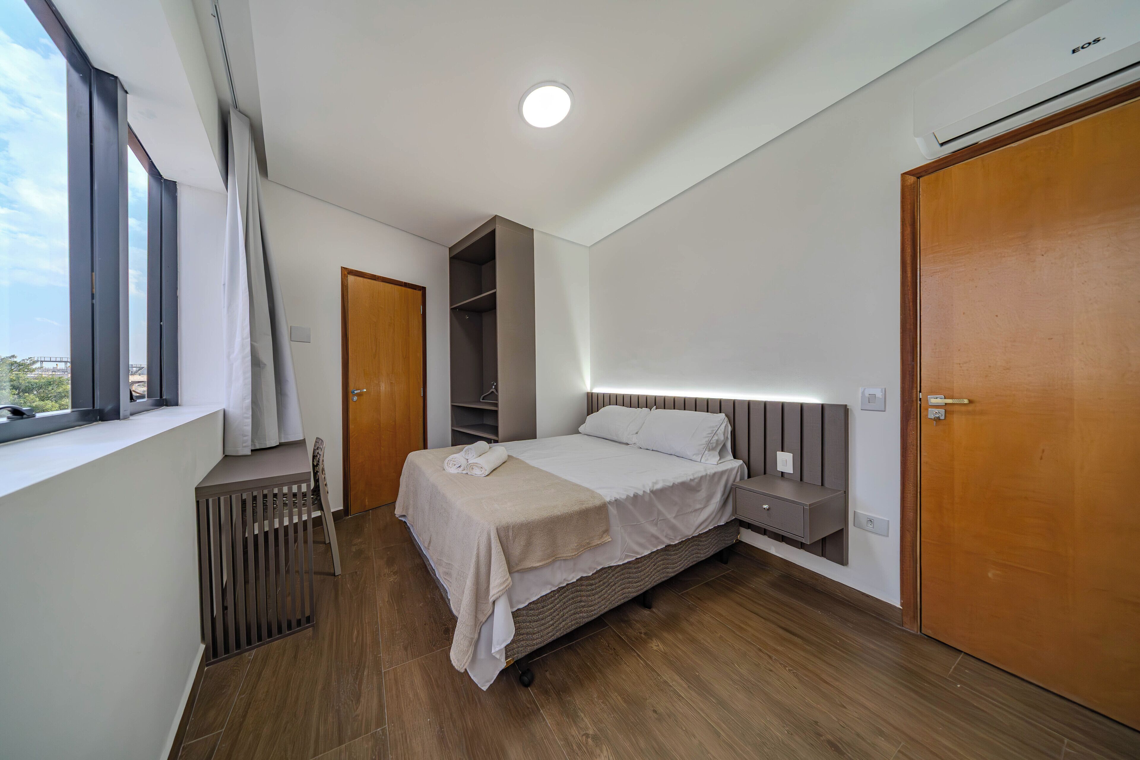 Een moderne slaapkamer met een bed, nachtkastjes, een kledingkast en een raam.