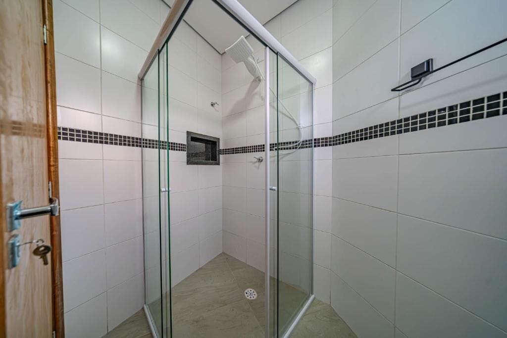 A glass-enclosed shower with white tiled walls and a small picture frame on the wall.