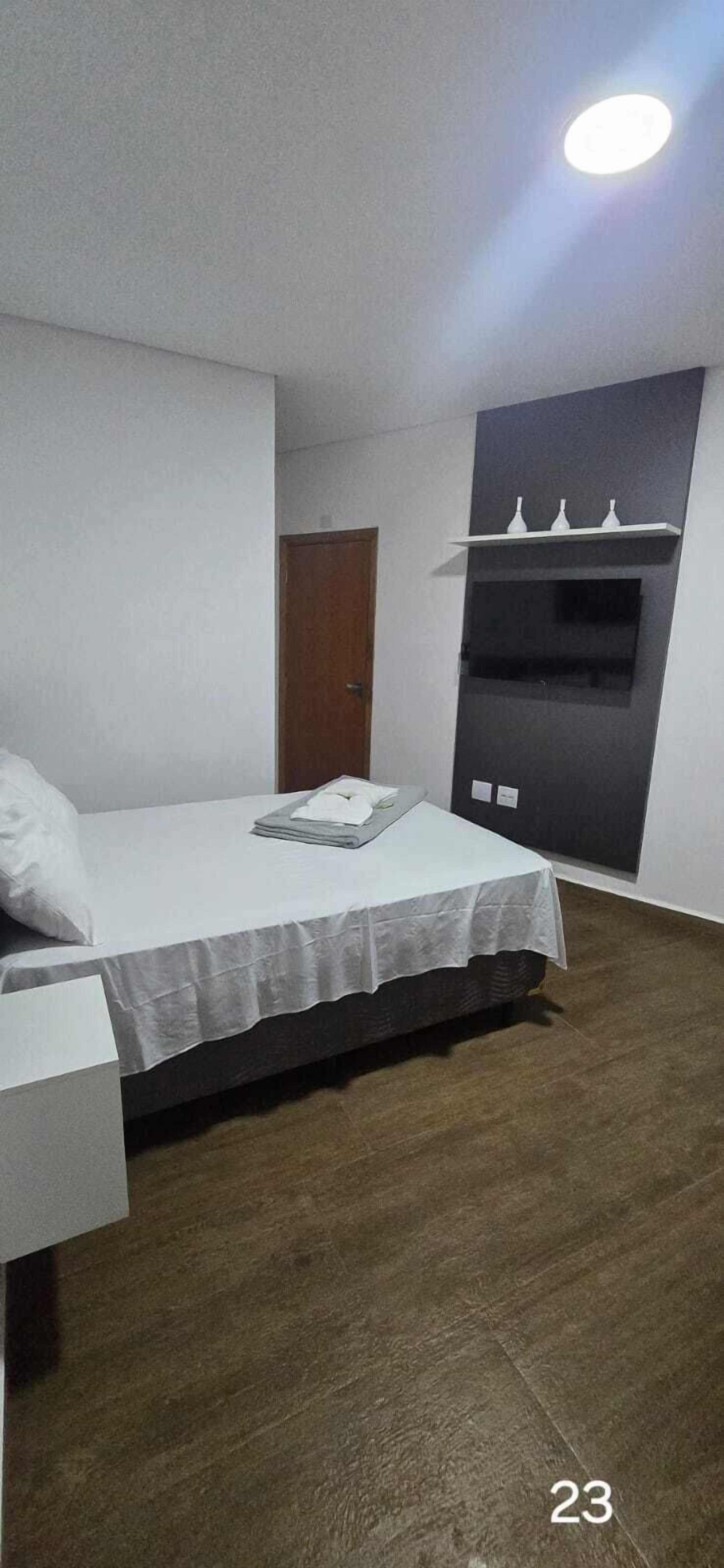 Ein Schlafzimmer mit einem Bett, einem Nachttisch, Holzboden, einer Tür und einem an der Wand befestigten Regal mit drei Vasen.