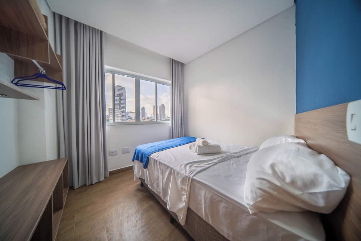 Ett hotellrum med en säng, en träbänk, ett fönster med utsikt över staden och en blå galge på väggen.