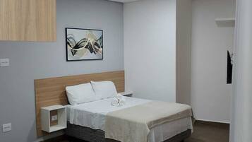 A modern hotel room with a wooden headboard, a neatly made bed, a small bedside table, and a framed abstract painting on the wall.