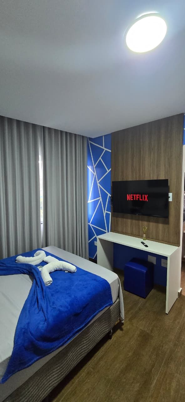 Habitació d'hotel amb llit, escriptori i televisió, i paret amb un dibuix geomètric.