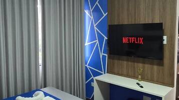 Habitació d'hotel amb llit, escriptori i televisió, i paret amb un dibuix geomètric.