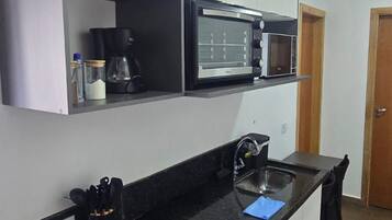 A compact kitchen with a black countertop, a built-in stove, a microwave, and a coffee maker.