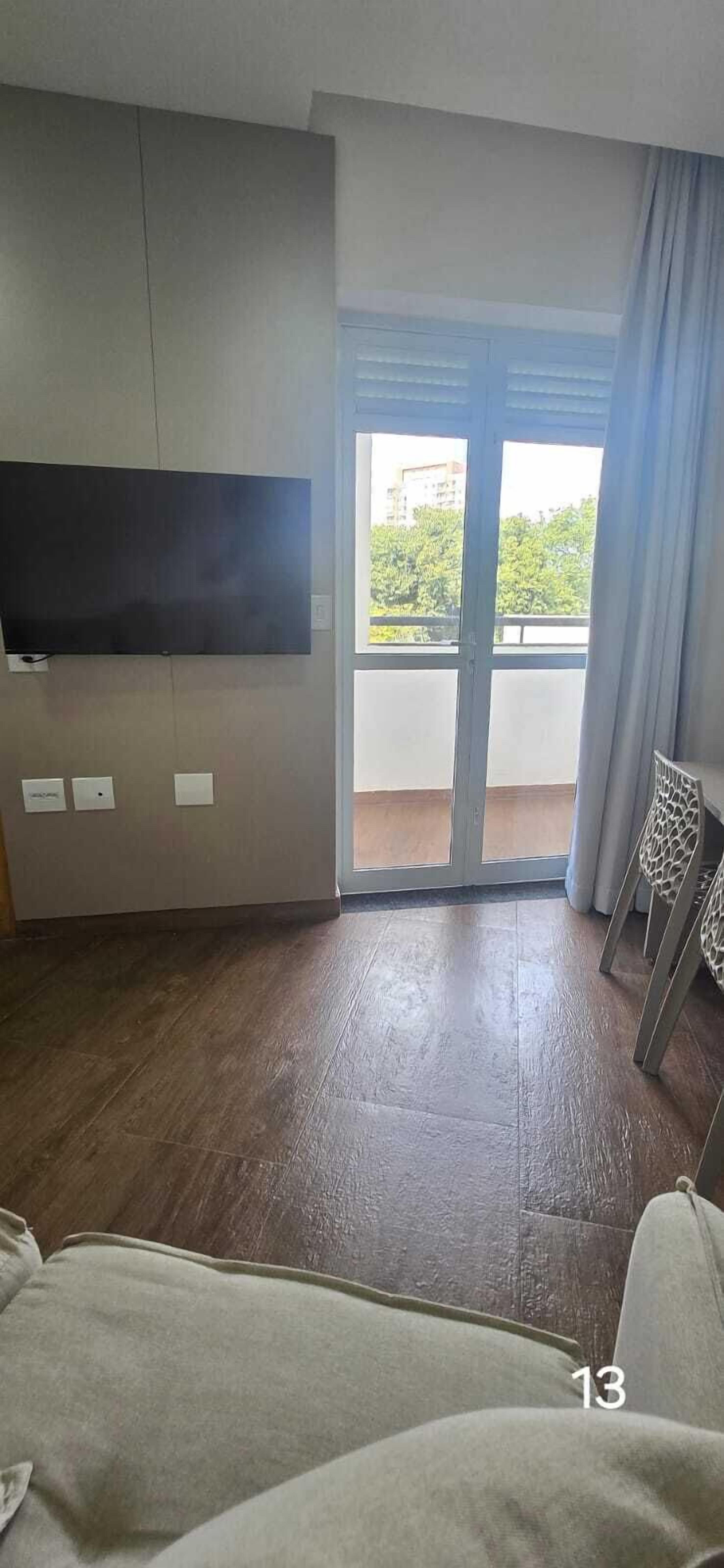 Una habitación con una televisión de pantalla plana montada en la pared, una puerta corrediza de vidrio que da a un balcón y una silla con estampado de jirafa.
