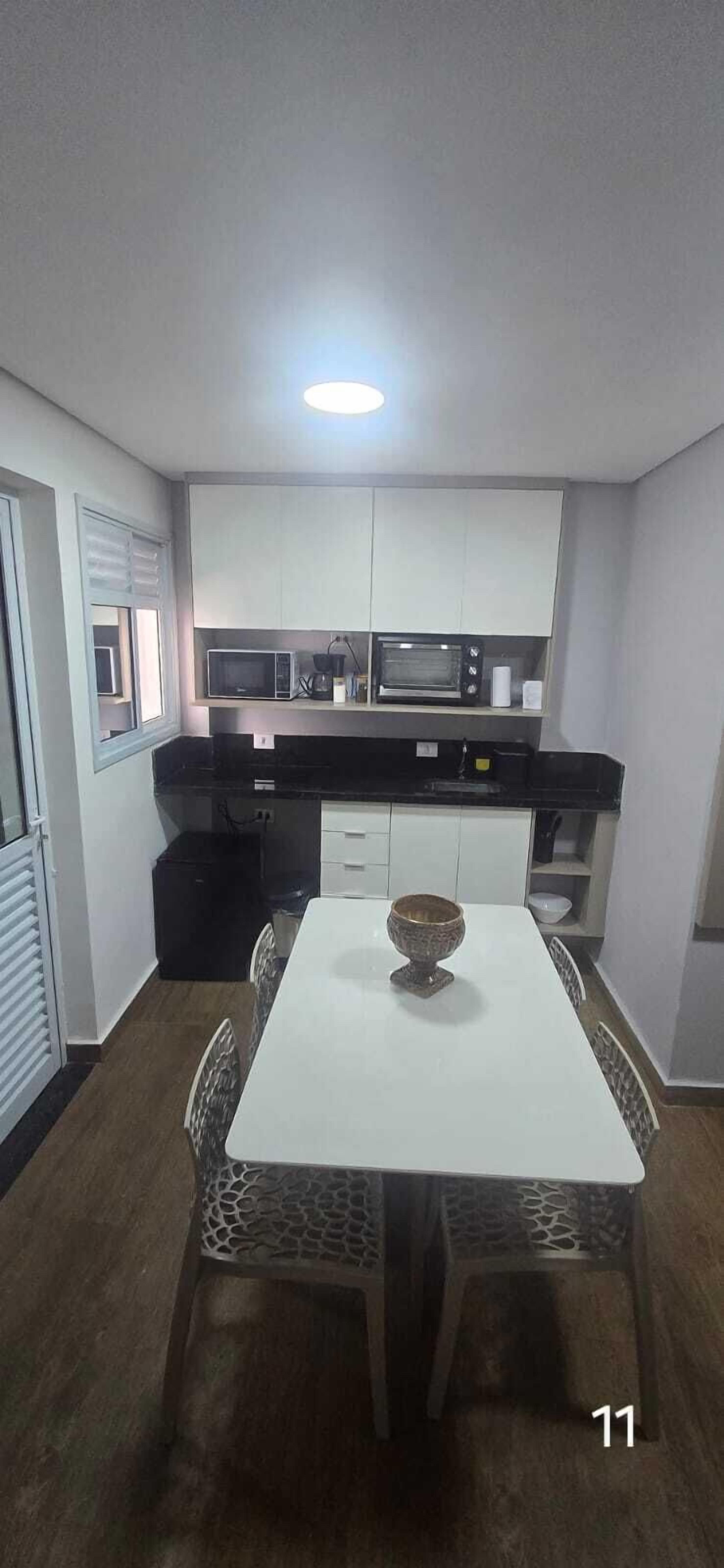 A compact kitchen with white cabinets, a black countertop, and a microwave. There is a dining table with a decorative bowl in the center.