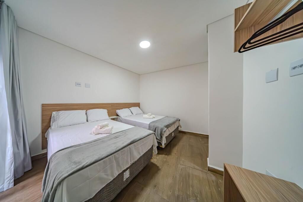 Een hotelkamer met twee enkele bedden, een houten hoofdbord, een klein houten bankje en een plafondlamp.