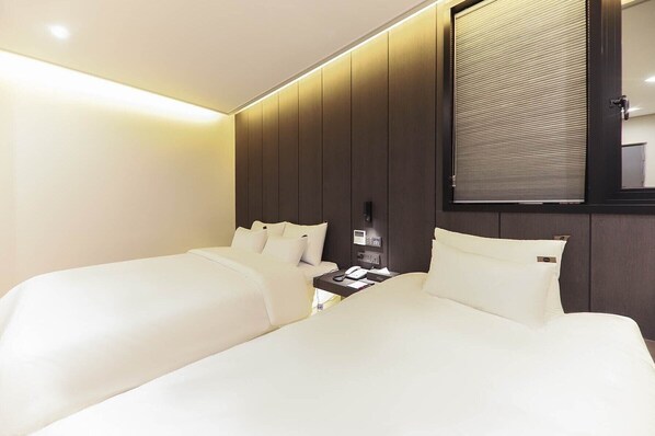A hotel room with two beds, a bedside table with a phone and a lamp, and a large window with blinds. - HOTEL SIGNATURE GWANGJU (Gwangju)