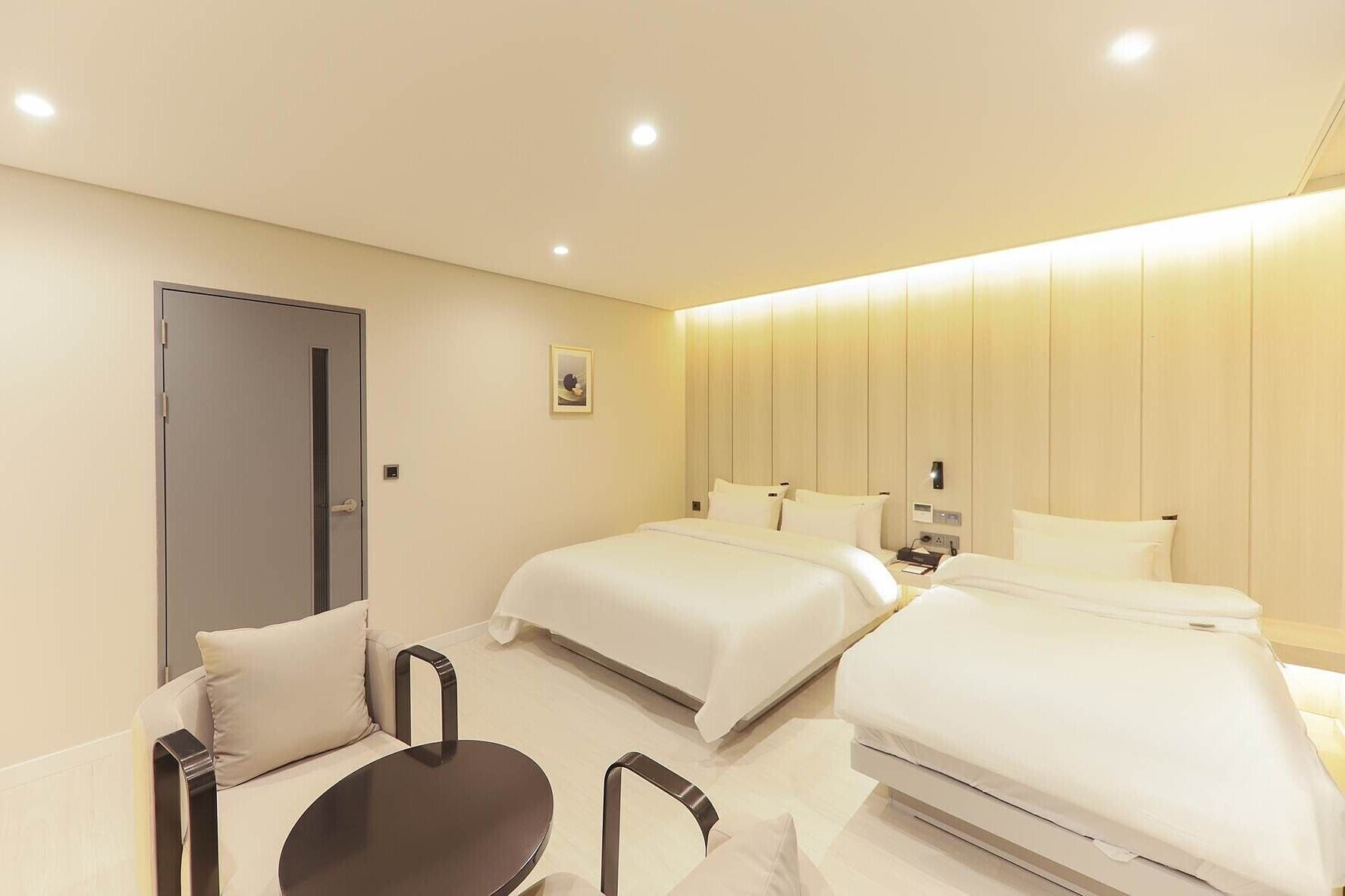 Ett modernt hotellrum med två sängar, en soffa, ett litet bord och en dörr.
