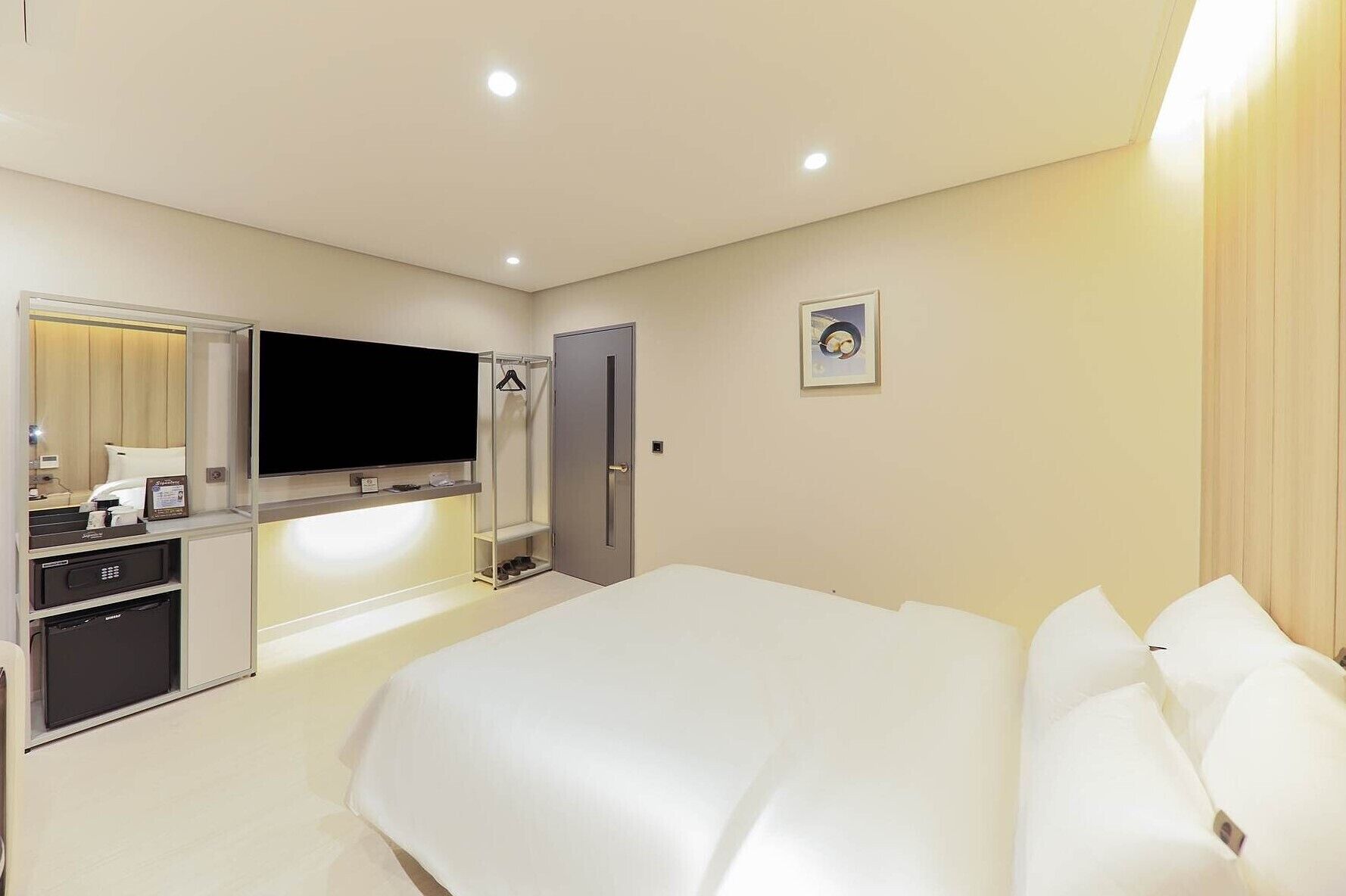 A hotel room with a large bed, a TV mounted on the wall, a wardrobe, and a small desk with a mirror.