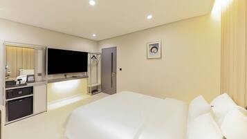 A hotel room with a large bed, a TV mounted on the wall, a wardrobe, and a small desk with a mirror.