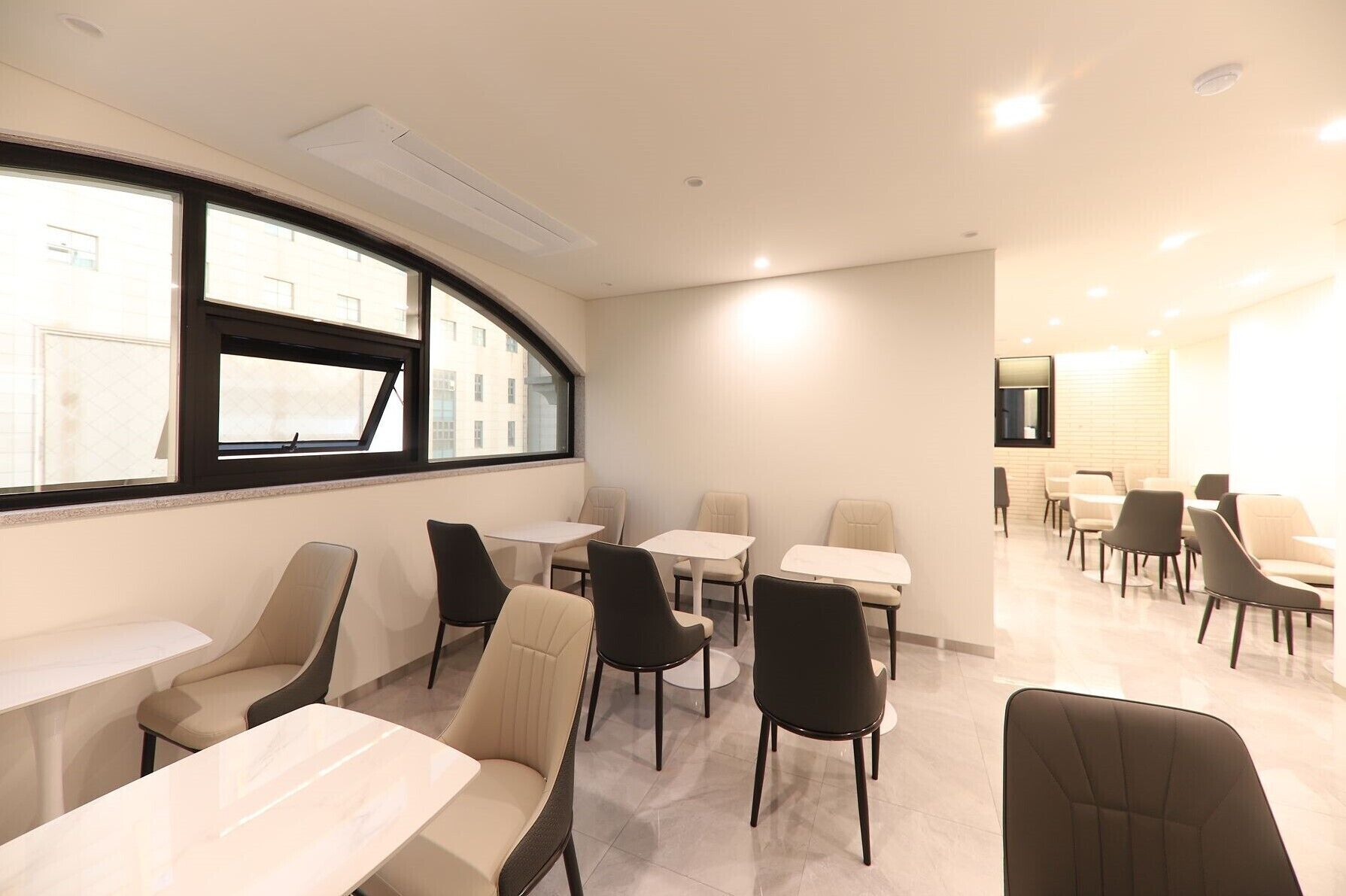 A modern dining area with round tables and chairs, large windows, and a clean, minimalist design.
