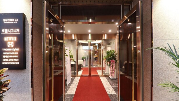 A hotel entrance with a red carpet, glass doors, and a sign listing amenities like a business center and breakfast. - HOTEL SIGNATURE GWANGJU (Gwangju)