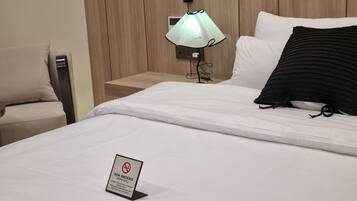A hotel room with a bed, a bedside table, a lamp, a chair, and a non-smoking sign.