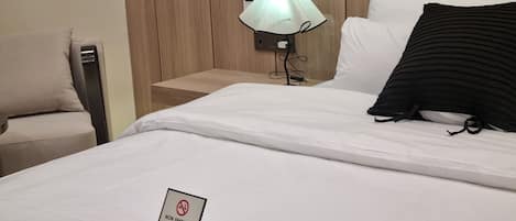 A hotel room with a bed, a bedside table, a lamp, a chair, and a non-smoking sign.