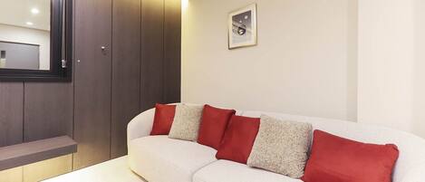 A modern living room with a white sofa, red and grey cushions, a wooden cabinet, and a framed picture on the wall.