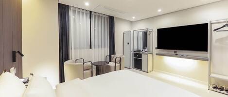 A modern hotel room with a large bed, a TV mounted on the wall, a desk with a chair, and a wardrobe.