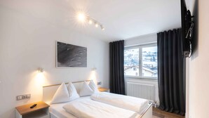 Ein modernes Hotelzimmer mit einem großen Bett, Nachttischen, einem wandmontierten Fernseher und einem Fenster mit Vorhängen.