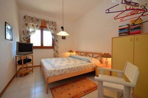 Ein Schlafzimmer mit Bett, Nachttisch, Lampe, Stuhl, Kleiderschrank, Fernseher und Vorhängen.