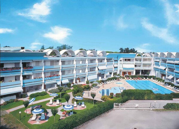 Ein mehrstöckiges Hotel mit einem zentralen Schwimmbecken, umgeben von Liegestühlen und Sonnenschirmen.