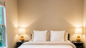 A bedroom with a bed, bedside lamps, a bench, and a window.