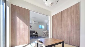 A modern room with a wooden table, a sofa, and a dining area visible through an open door.