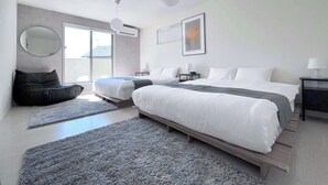 A modern hotel room with a large bed, a seating area with a round mirror, and a view of the outdoors through a sliding door.