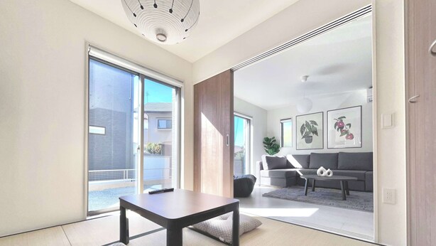 A modern living room with tatami mats, a sofa, a coffee table, and a sliding glass door leading to a balcony.