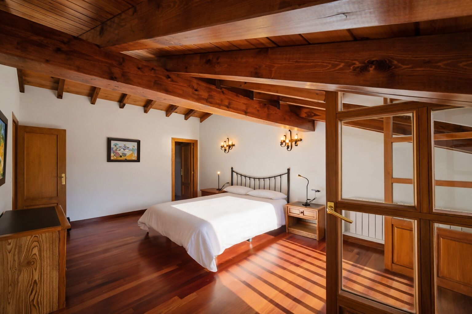 Ein Schlafzimmer mit Holzboden, einem Bett, einem Nachttisch und einer Wandleuchte.