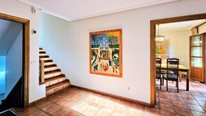 A hallway with a tiled floor, a staircase, a dining area with chairs and a table, and a wall-mounted painting. - La Franca beach, garden and WiFi - Casa Freya (Franca, La)