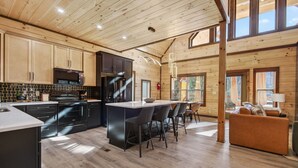 Una cucina moderna con mobili in legno, un'isola centrale con sgabelli da bar e un'area pranzo con divano e tavolo.