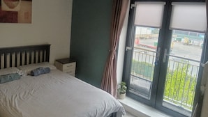 A bedroom with a bed, a nightstand, a window with curtains, and a view of a parking lot. - Cheap modern room (Dublin)