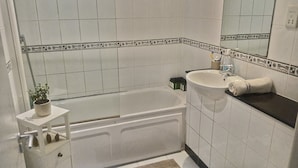 A bathroom with a bathtub, sink, and toilet. There is a small shelf with a potted plant and a towel on the counter. - Cheap modern room (Dublin)