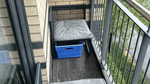 A balcony with a metal railing, a blue crate, and a grey cushioned bench. - Cheap modern room (Dublin)