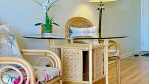 A round glass table with a woven chair, a potted orchid, and a lamp. - Bright condo in beautiful Honolulu with cool AC breeze (Honolulu)