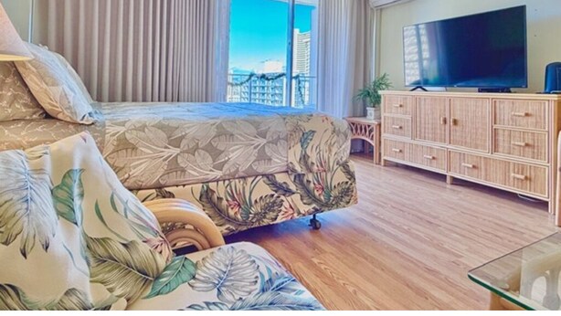 A bedroom with a bed, a TV, a wooden cabinet, and a window with a view. - Bright condo in beautiful Honolulu with cool AC breeze (Honolulu)