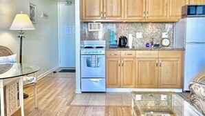 A compact kitchen with wooden cabinets, a stove, a microwave, and a refrigerator. - Bright condo in beautiful Honolulu with cool AC breeze (Honolulu)