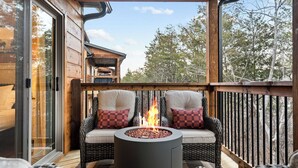 Een houten terras met rieten meubilair en een vuurkorf in het midden.