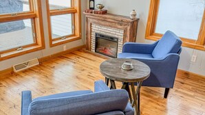 Una sala de estar acogedora con chimenea, ventanas amplias y vistas a un paisaje nevado.